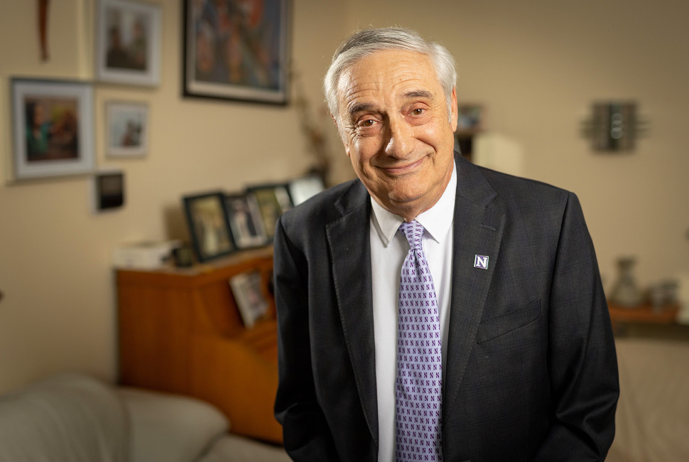 Joel Mokyr smiles in his office wearing a suit and Northwestern pin